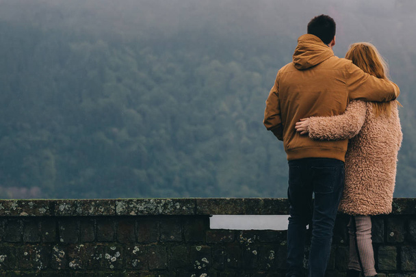 O tipo abraça uma rapariga e admiram as montanhas. vista para trás
 - Foto, Imagem