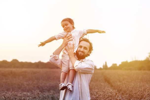 father's day. Dad and son playing together outdoors on a summer. Happy family, father, son at sunset. The concept of organic farming and healthy lifestyle,  happiness and joy - Фото, изображение