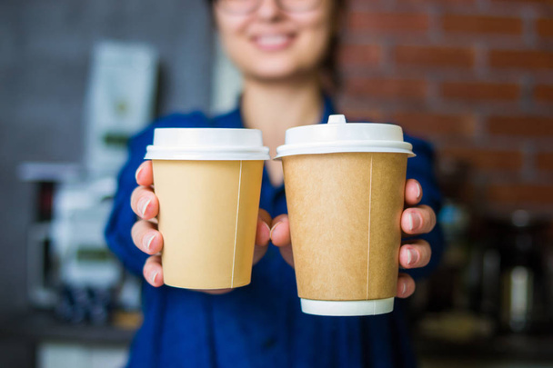 jovem sorridente barista menina estende as mãos com uma xícara de papel de café para ir com espaço para o logotipo
 - Foto, Imagem