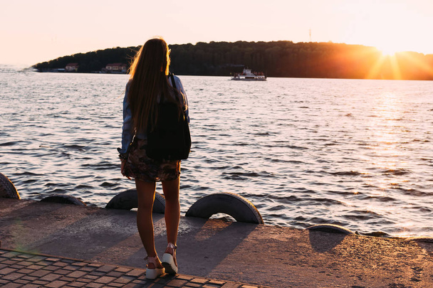 Дівчина на березі озера захоплюється заходом сонця і кораблем
 - Фото, зображення