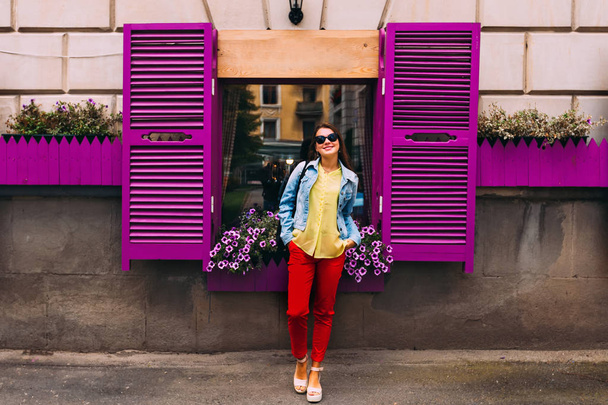 Стильна дівчина з сонцезахисними окулярами біля фіолетового вікна з жалюзі
. - Фото, зображення