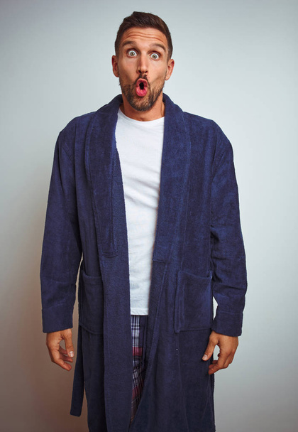 Young man wearing comfortable pajamas and robe at morning over isolated background afraid and shocked with surprise expression, fear and excited face. - Foto, imagen