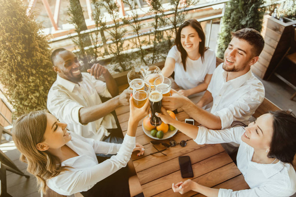 Young group of friends drinking beer and celebrating together - Фото, изображение