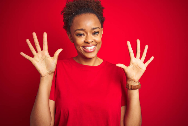 İzole kırmızı arka plan üzerinde afro saç ile genç güzel Afrikalı Amerikan kadın gösteren ve parmak numarası on ile işaret kadar güven ve mutlu gülümseyen. - Fotoğraf, Görsel