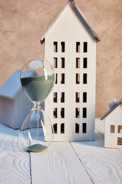houses models and hourglass on white wooden table near textured wall, real estate concept - 写真・画像