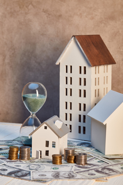 houses models and hourglass on cash and coins, real estate concept - Valokuva, kuva