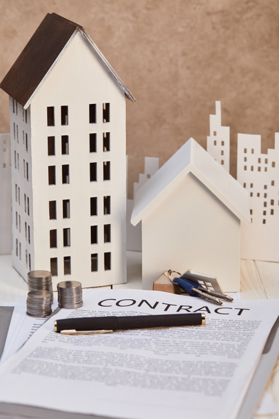 houses models on white wooden table with contract, keys and coins, real estate concept - Photo, Image