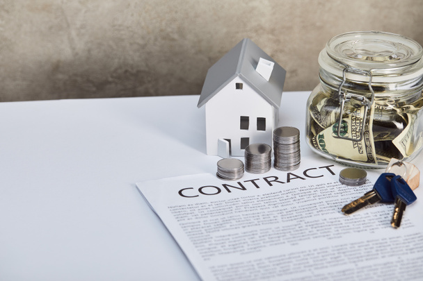 modelo de casa en mesa blanca con monedas de plata, llaves, contrato y caja de dinero, concepto de bienes raíces
 - Foto, Imagen