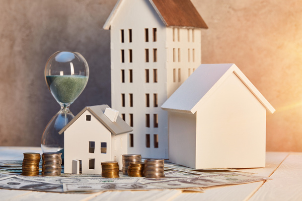 houses models, coins and cash, hourglass on white wooden table with sunlight, real estate concept - Photo, Image