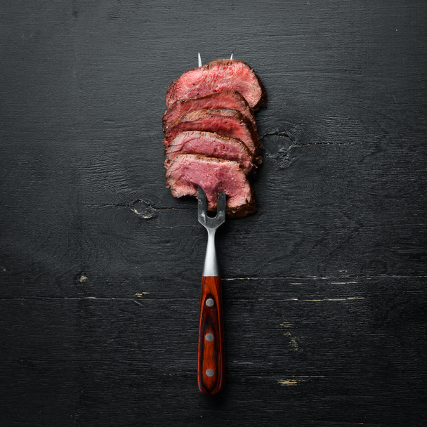 Beef steak on a fork. On a wooden background. Top view. Free space for your text. - Foto, imagen