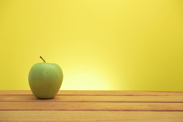 Vihreä omena punaisella puupöydällä, keltainen tausta
. - Valokuva, kuva