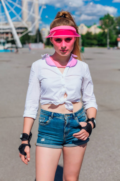 Portrait of an emotional girl in a pink cap visor and protective gloves for rollerblades and skateboarding. - Foto, Imagem
