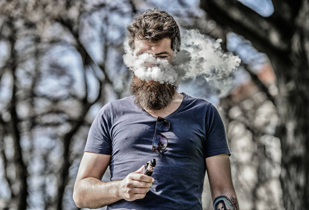 Bearded man smoking vape. Smoking electronic cigarette. Man long beard relaxed with smoking habit. Man with beard and mustache breathe out smoke. White clouds of flavored smoke. Stress relief concept - Foto, imagen