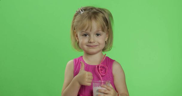 Feliz niño de cuatro años en vestido rosa con cóctel batido. Pulgares arriba
 - Foto, Imagen