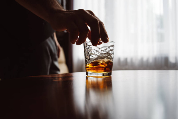Close up of man's hand holding glass of whiskey. Tasting and degustation concept. Businessman in elegant suit with glass of whiskey. Place for text - Photo, Image