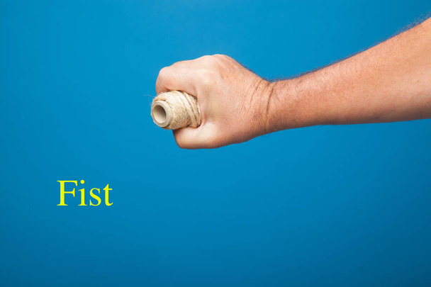 Right hand fist holding a roll of string or rope on blue background - Photo, Image