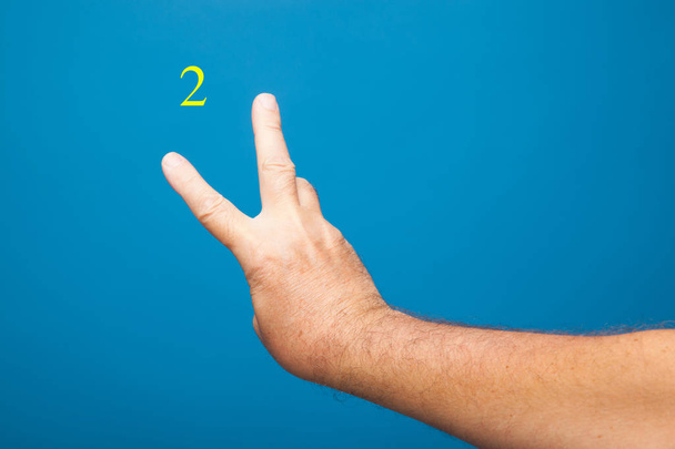Käsi ja sormet tehdä merkkejä ja numeerisia symboleja ja suljettu nyrkki tavallisella taustalla. Nyrkki mies tekee numeroita sormilla
. - Valokuva, kuva
