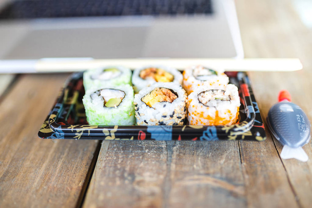 Several tasty sushi rolls and laptop at wooden table - Fotoğraf, Görsel