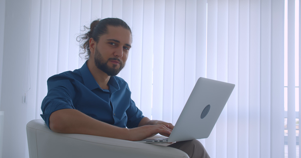 Profil strzał współczesnego Freelancer wpisując na laptopie siedzi w fotelu w biurze w świetle zamienia się w kamerę i zegarki uśmiechając. - Materiał filmowy, wideo