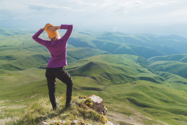 Hátulsó kilátás egy vonzó női turista állt egy füves dombon visel napszemüveg. Élvező nyári napsütéses napon a Kaukázusban. Aktív idegenforgalomra vonatkozó koncepció - Fotó, kép