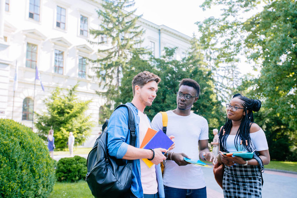 Három pozitív diákok különböző coupróbálkozás a könyvek és hátizsákok beszél, miközben gyalog épület ellen egyetemi campus kültéri. Új tanév koncepció. - Fotó, kép