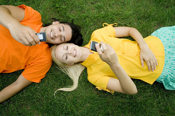 Coppia sdraiata sull'erba con telefoni cellulari
 - Foto, immagini