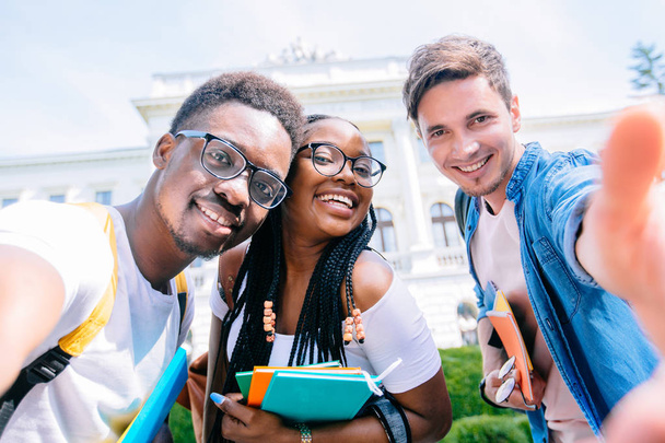 Afrohaarmädchen mit Brille macht Selfie mit ihren besten Freundinnen im Freien. fröhliche multiethnische Studentengruppe, die Spaß mit Smartphone-Fotokamera hat. - Foto, Bild