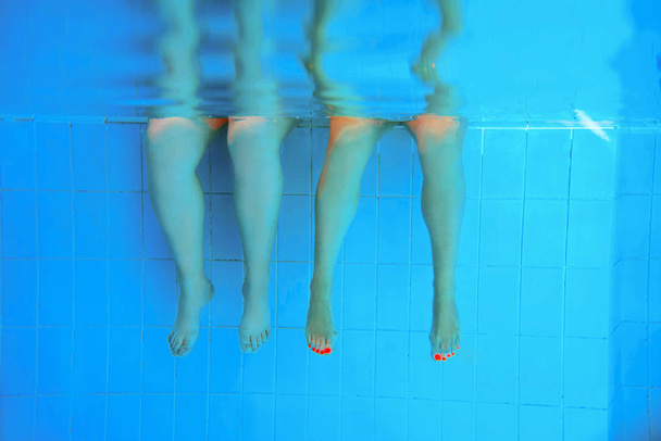 two people legs (caucasian persons) underwater in the swimming pool. Party. Summer. Vacation, diversity, friendship and sport concept. - Фото, изображение