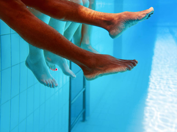 水中のスイミングプールで白人の友人とアフリカ系アメリカ人の男性の足。夏。バケーション、インターナショナル、スポーツのコンセプト. - 写真・画像