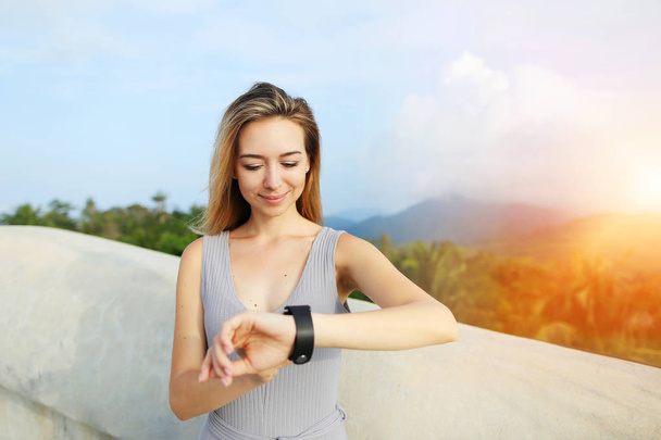 Sol retrato de mujer rubia joven usando smartwatch, montañas en el fondo, Tailandia
. - Foto, imagen