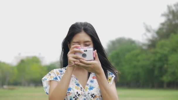 公共の公園で屋外でおもちゃのカメラで写真を撮って楽しむスローモーション美しいアジアの女性. - 映像、動画