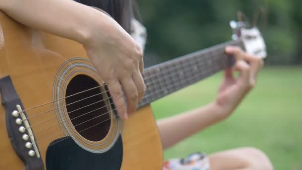 Slow-Motion close-up van jonge vrouw met de hand gitaar spelen buitenshuis in een openbaar park. - Video