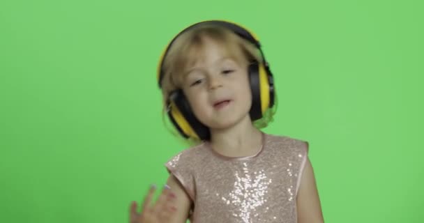 Dziewczynka w błyszczącej sukni i słuchawkach słuchania muzyki i tańca. Klucz chrominancji - Materiał filmowy, wideo