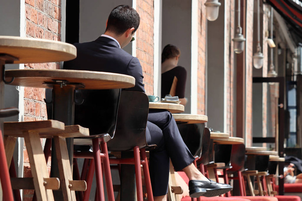 Young man in a business suit sitting at a table in street cafe. Concept of lunch alone, waiting for a date or business meeting, coffee break - Photo, Image