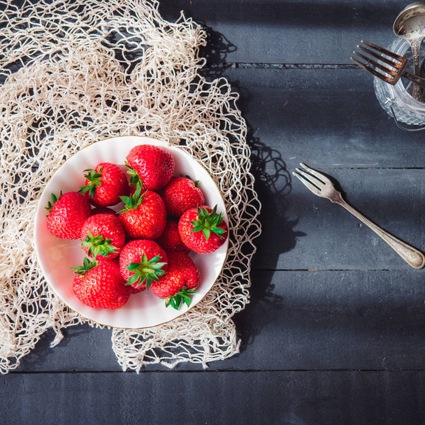 Freshly picked juicy organic strawberries in ceramic bowl on rustic black wooden kitchen table lightened by morning window light. Farmer harvest, local market. Selective focus, Copy space. Flat lay. - Фото, зображення