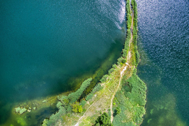 eine kleine Landzunge mit einem Pfad, der auf beiden Seiten mit grünem Gras bedeckt ist, an einem klaren See. Luftaufnahmen - Foto, Bild