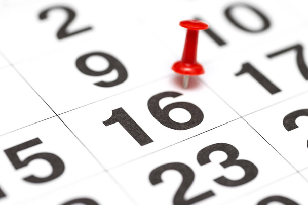 PIN op het datum nummer 16. De zestiende dag van de maand is gemarkeerd met een rode Thumbtack. PIN op kalender - Foto, afbeelding