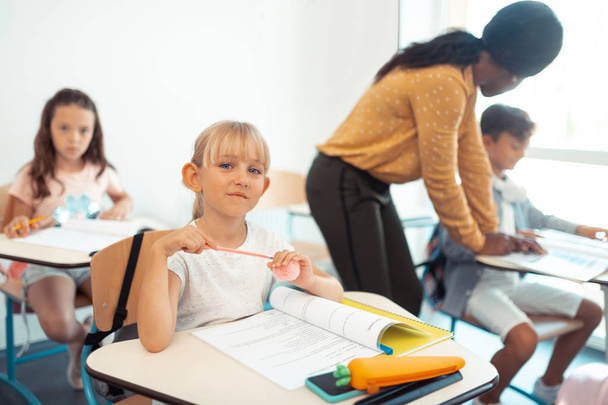 Красива блакитноока школярка сидить за столом в класі
 - Фото, зображення