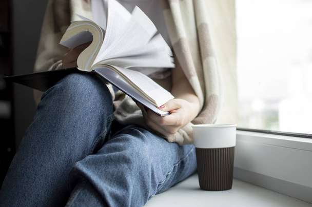 junges Mädchen mit Decke sitzt zu Hause am Fenster, liest ein Buch und trinkt Tee, kopiert Platz für Text - Foto, Bild