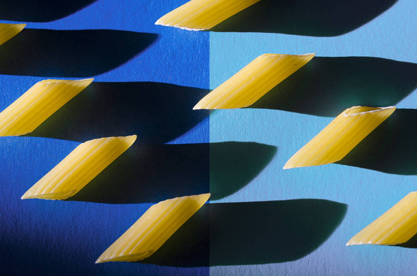 Penne pasta is een scherpe schaduw tegen een gekleurde achtergrond - Foto, afbeelding