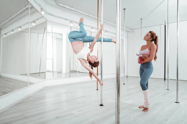 Woman watching her friend doing pole exercises. - Foto, imagen