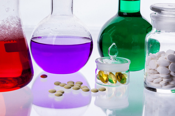 Vidraria de laboratório com líquidos de diferentes cores e tablet
 - Foto, Imagem