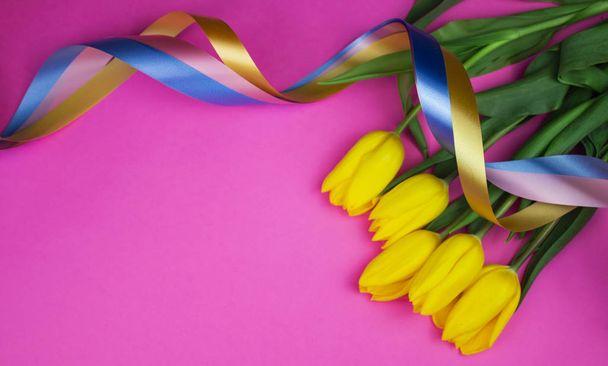Tulipanes amarillos con cintas de colores sobre un fondo rosa. flor
  - Foto, Imagen