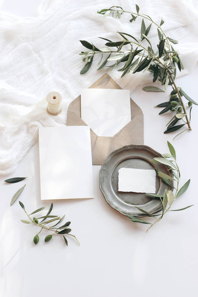 Summer wedding stationery mock-up scene. Blank greeting cards, envelope, vintage silver plate, olive branches and ribbon. White background with cotton table runner in sunlight. Flat lay, top view. - Valokuva, kuva