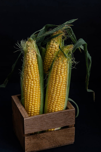 Yellow sweet raw corn in a wooden box on a black background clos - Zdjęcie, obraz