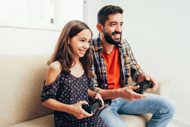Smiling father and daughter playing video game at home - Fotó, kép