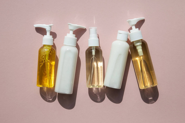A collection of beauty cosmetic producs in clear bottles on a pink background - 写真・画像