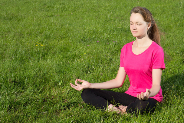 Young woman siiting on the grass in yoga pose - Photo, Image