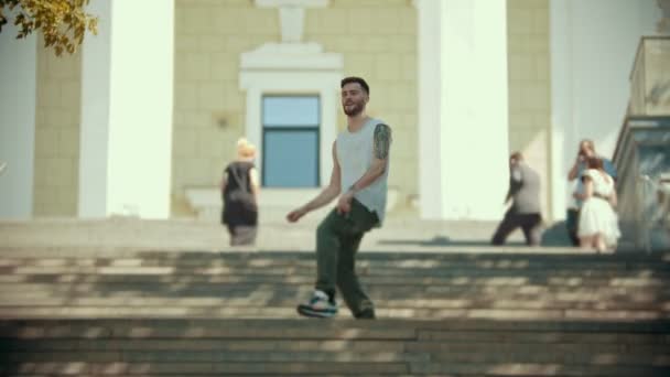 Jovem e elegante homem feliz com tatuagens dançando nas escadas em um fundo de um edifício
 - Filmagem, Vídeo