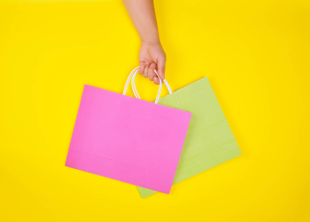 el sarı bir arka plan üzerinde iki kağıt alışveriş torbaları tutarak - Fotoğraf, Görsel